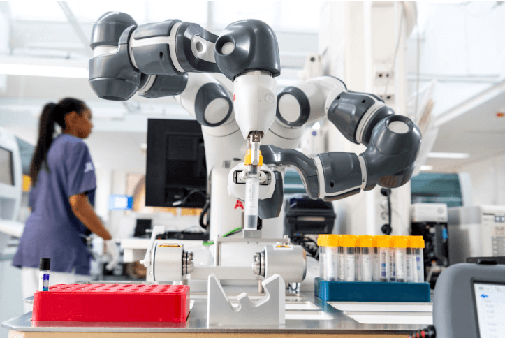 Dual-arm laboratory robot handling sample tubes while a technician works nearby