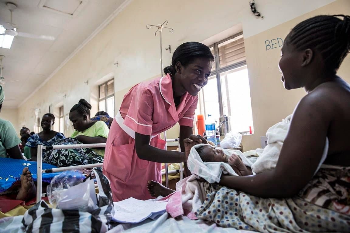 Nurse caring for a patient in a busy hospital ward